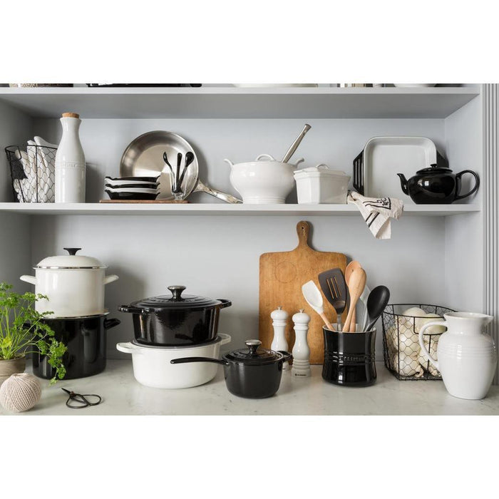 An assortment of Le Creuset cookware displayed on a white countertop and shelf