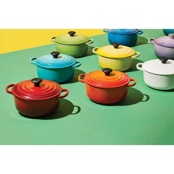 An assortment of colorful Le Creuset 1 qt Enameled Cast Iron Signature Round Dutch Oven with lid displayed on a green surface