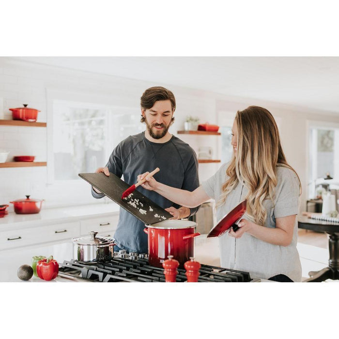 2 individuals scrapping onions into a Cerise Le Creuset 16 Qt. Enamel on Steel Stockpot in a kitchen setting