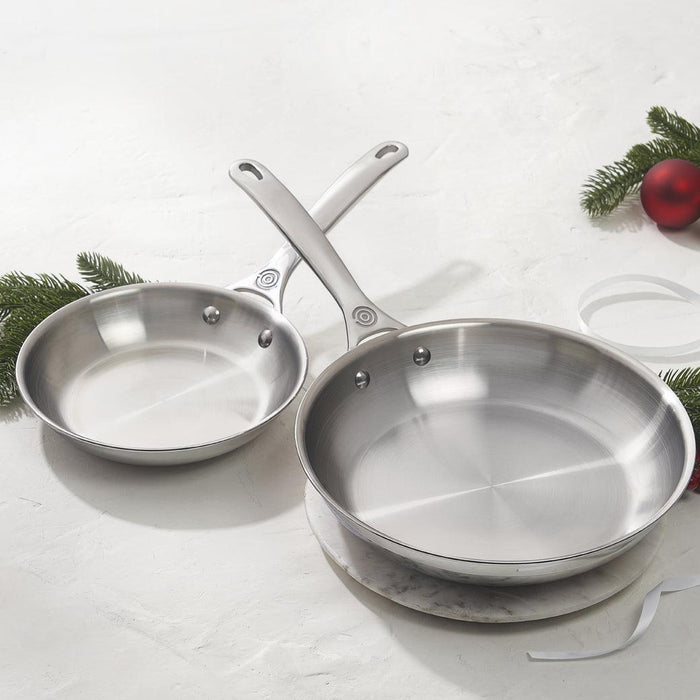 Le Creuset 2 Piece Set (8″ Fry Pan & 10″ Fry Pan) placed on a marble trivet next to pine needle branches displayed on a white surface