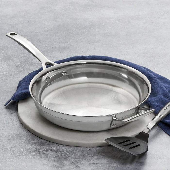 Le Creuset Fry Pan placed on a marble trivet next to a blue towel and spatula displayed on a marble surface