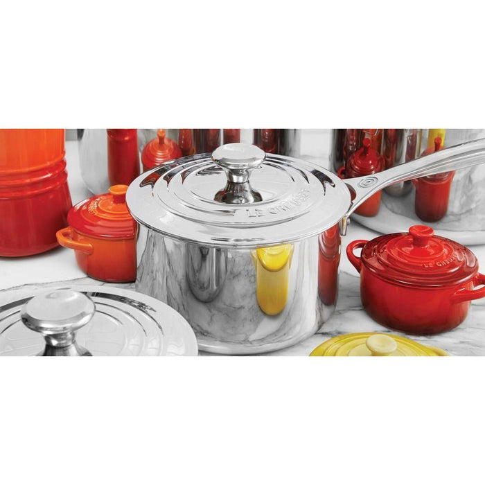 Le Creuset 2 Qt. Stainless Steel Saucepan with Lid next to other Le Creuset cookware on a marble countertop