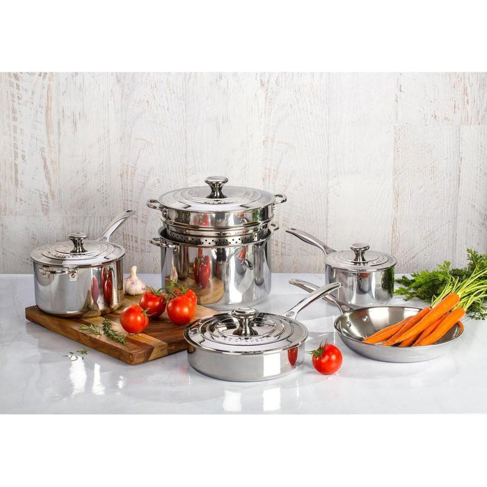 Le Creuset Stainless Steel cookware next to cutting board and vegetables on a white countertop