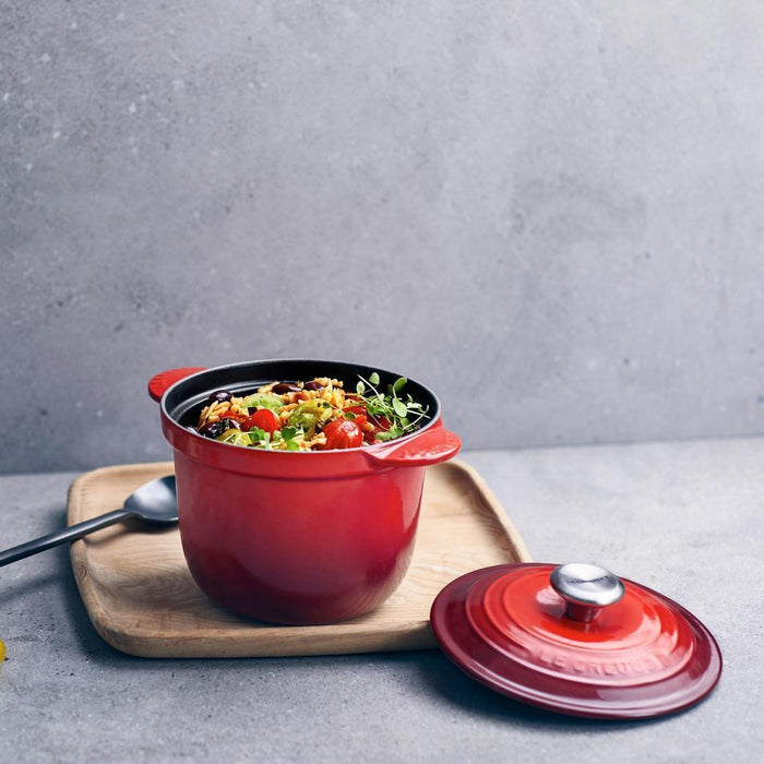 Cerise Le Creuset 2.25 qt Rice Pot with Stoneware Insert with rice dish inside placed on a wooden board on a cement surface