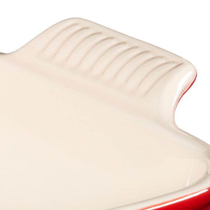 Close up of handle Cerise Le Creuset 3 qt Heritage Square Dish displayed on a white background