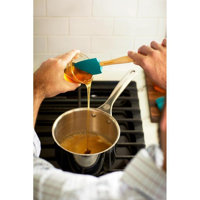 Honey being poured into a Le Creuset stainless steel saucepan on a stove