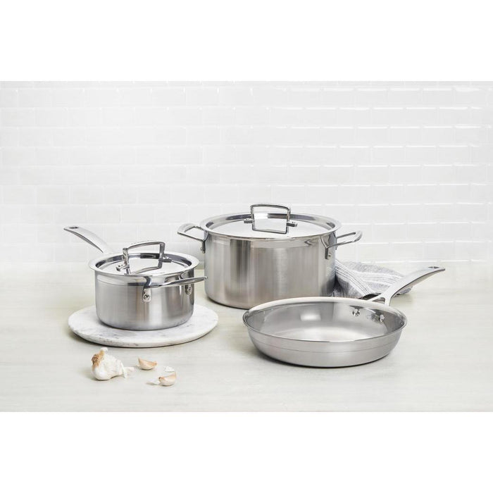 Le Creuset 4 Qt. Stainless Steel Saucepan displayed with other pans and garlic on a grey counter