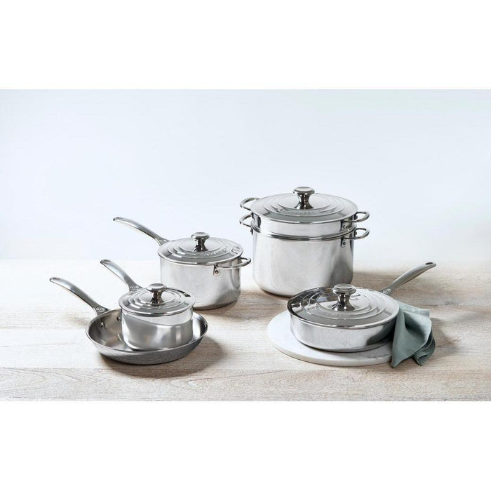 Le Creuset 4 Qt. Stainless Steel Saucepan with Lid displayed with other pans on a stone countertop