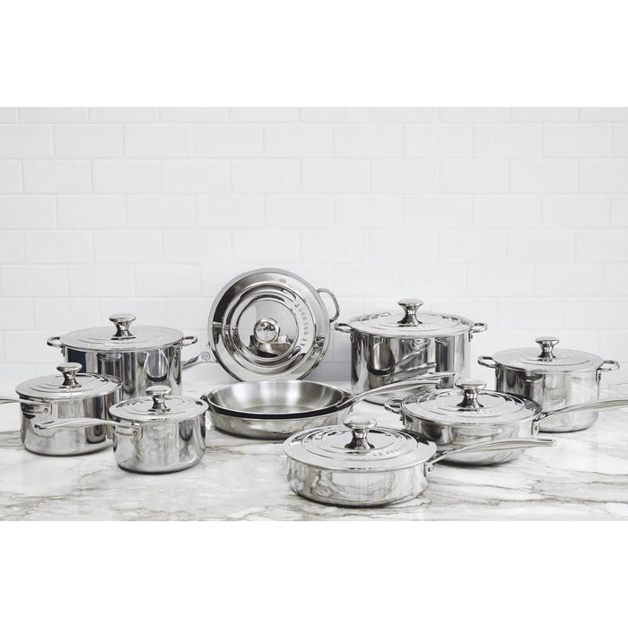 Collection of stainless steel pots and pans from Le Creuset on a marble countertop
