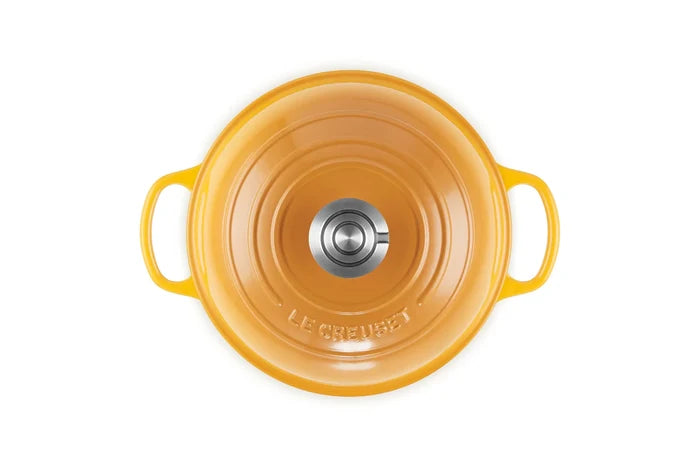 Top-down view of a Le Creuset enameled cast iron pot in a vibrant orange-yellow color, featuring two side handles and a stainless steel knob on the lid, set against a plain white background.