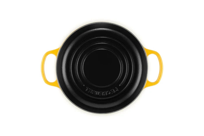 A Le Creuset black cast iron casserole dish with bright yellow handles, shown from a top-down view on a white background.