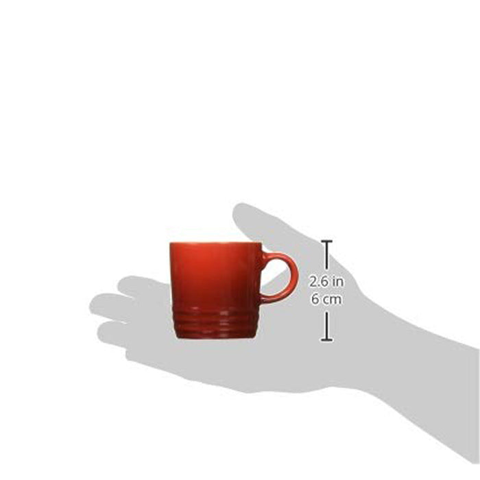 Someone holding 3 oz. Cerise Le Creuset Stoneware Espresso Mug with dimensions displayed on a white background