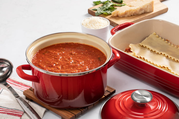 Cerise 3.8 qt enamel on steel traditional petite stockpot with lid and handles with  food inside next to casserole with noodles and cheese beside it on a white countertop