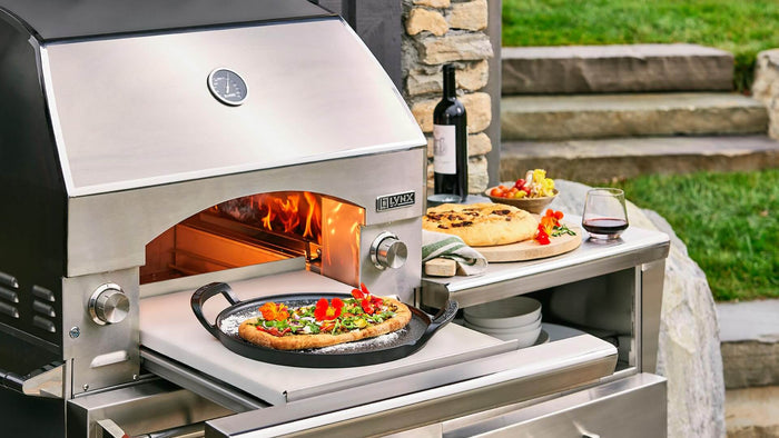 Outdoor pizza oven with a pizza being cooked, surrounded by outdoor furniture and decor.
