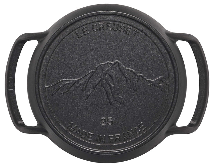 Black cast iron lid with mountain design and 'Le Creuset' branding on a white background