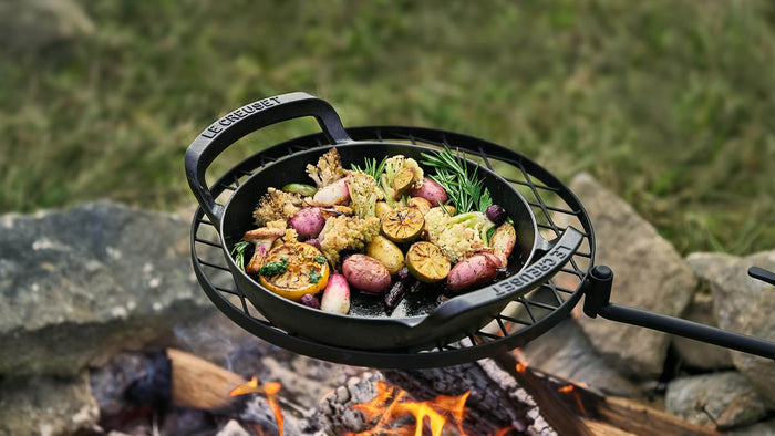 Black cast iron skillet with roasted vegetables over a campfire