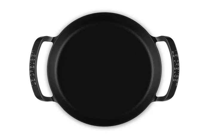 A black cast iron utility pan with two side handles, photographed from a top-down perspective on a solid white background.