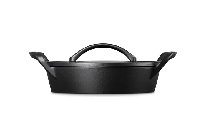 A black cast iron Dutch oven with a lid and integrated top handle, shown from a front three-quarter angle on a solid white background.