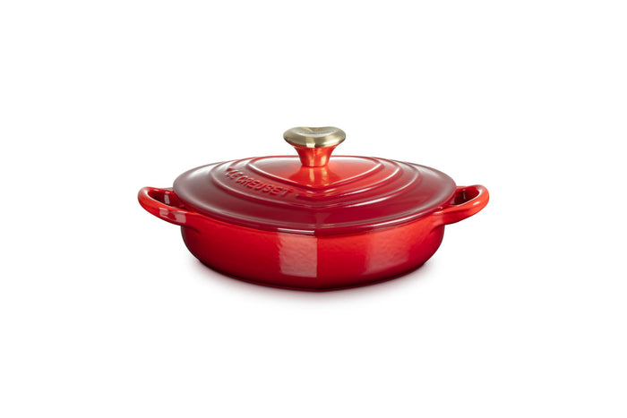 Side view of cerise heart shaped 1.25 qt cocotte with handles and a light gold heart knob displayed on a white background