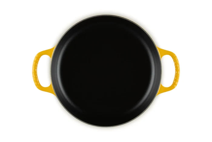 A top-down view of a round black cast iron skillet with bright yellow handles, isolated on a white background.