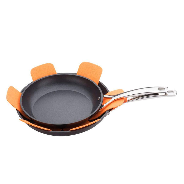 An orange Le Creuset Felt Pan Protector being used to protect 2 skillets that are stacked on each other on a white background