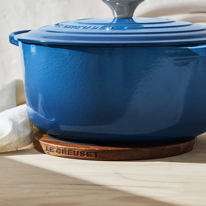 Blue Le Creuset pot on top of the Le Creuset magnetic wooden trivet on a wooden table