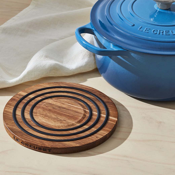 Le Creuset magnetic wooden trivet next to a white cloth and blue Le Creuset pot on a wooden surface