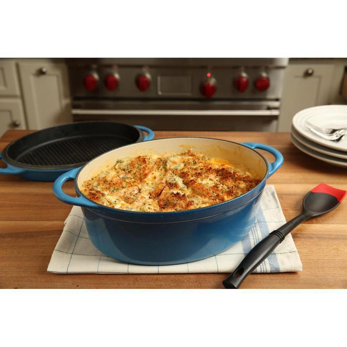 Cerise Le Creuset Revolution Bi-Material Saute Spoon next to blue Le Creuset cookware with baked casserole placed in a kitchen setting