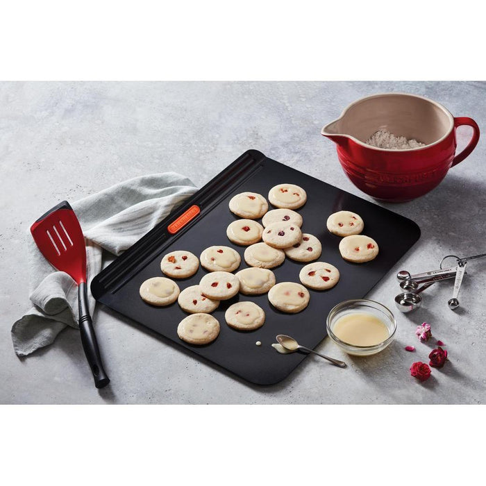 Le Creuset Revolution Bi-Material Slotted Turner with cookies and cooking materials on a grey surface