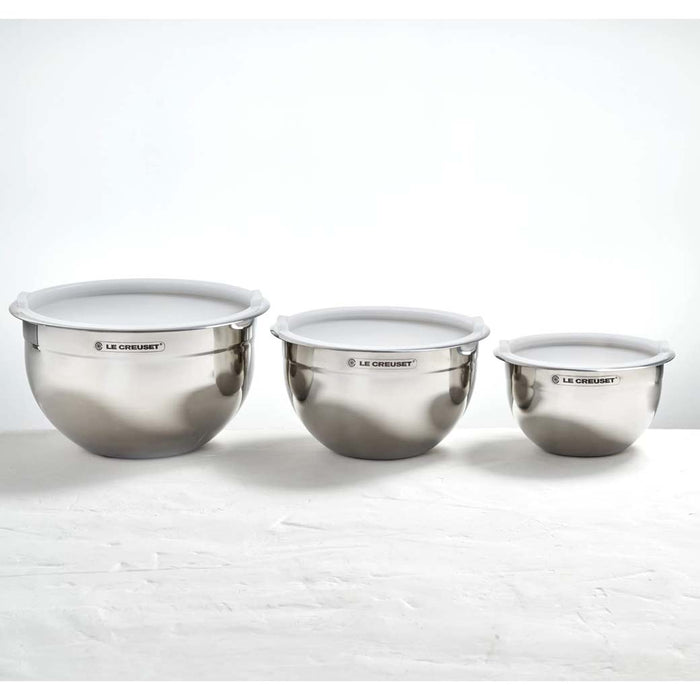 Set of 3 Le Creuset stainless steel mixing bowls with lids displayed in a row on a white surface