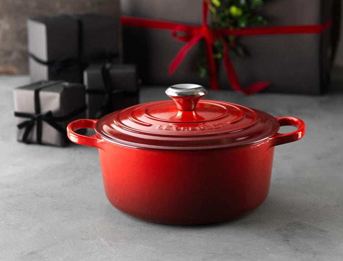 Le Creuset Signature Stainless Steel Knob on a cerise Le Creuset pot and lid with a blurred out background of black wrapped packages