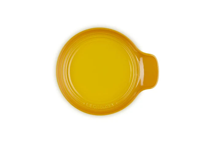 A round yellow ceramic spoon rest with a small side handle, photographed from directly above on a white background.