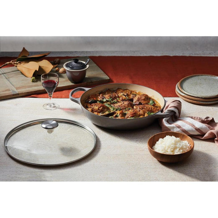 12 inch Le Creuset Signature Tempered Glass Lid next to a pan with cooked food on a wooden surface