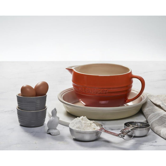 Cerise Le Creuset Stainless Steel Measuring Cups next to baking materials on a marble surface