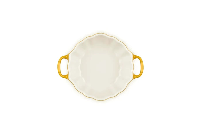 A white ceramic baking dish with a scalloped rim, two yellow handles, and a yellow-gold rim, shown from a top-down view on a white background.