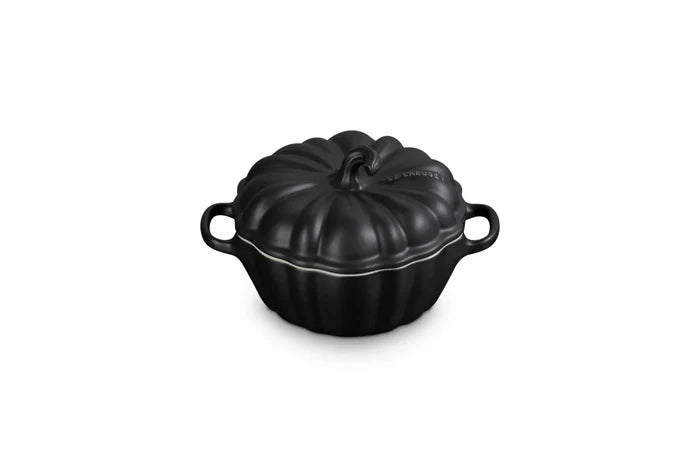 A black cast iron pumpkin-shaped lidded cocotte dish with side handles, shown on a solid white background.
