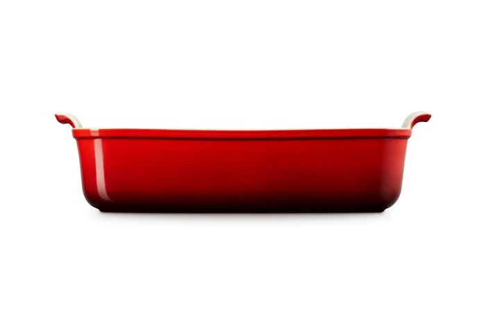 Side view of a red rectangular baking casserole dish with two small loop handles on the sides, shown from a front-facing perspective on a solid white background.