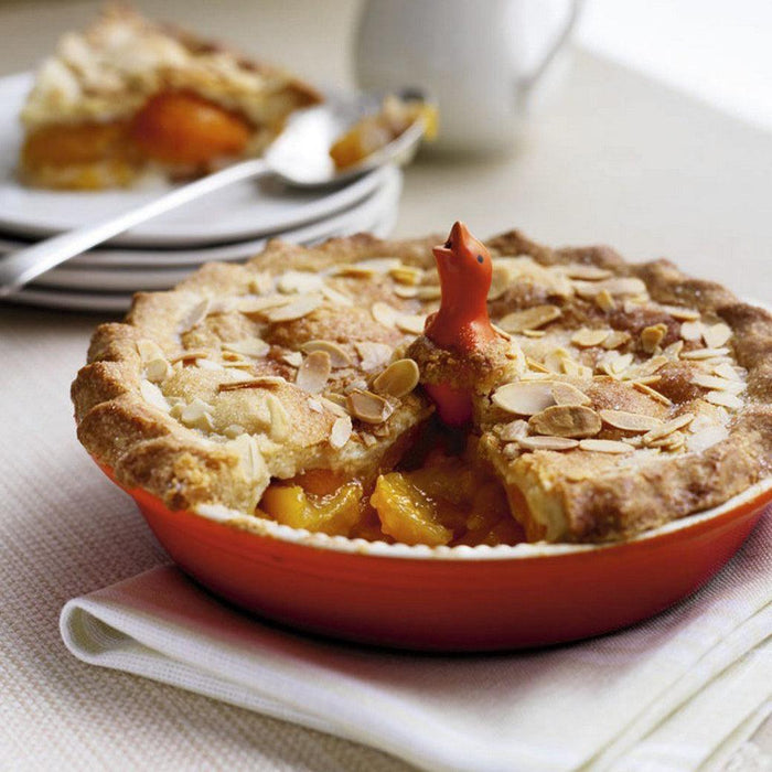 Flame Le Creuset Stoneware Pie Bird placed in the middle of a peach pie on a tabletop