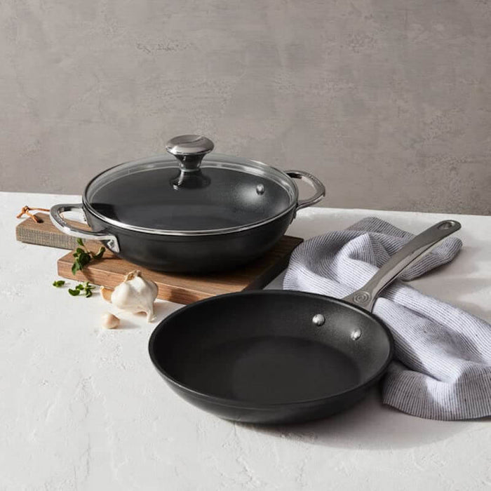 Black cookware set with a frying pan and a covered pot on a light surface.