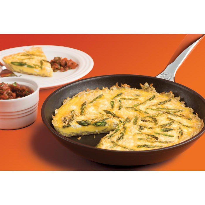Le Creuset Toughened Nonstick PRO Fry Pan with a egg pie next to a plate with a slice of egg pie and some salsa displayed on an orange background