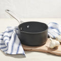 Black saucepan on a wooden cutting board with garlic and a striped cloth