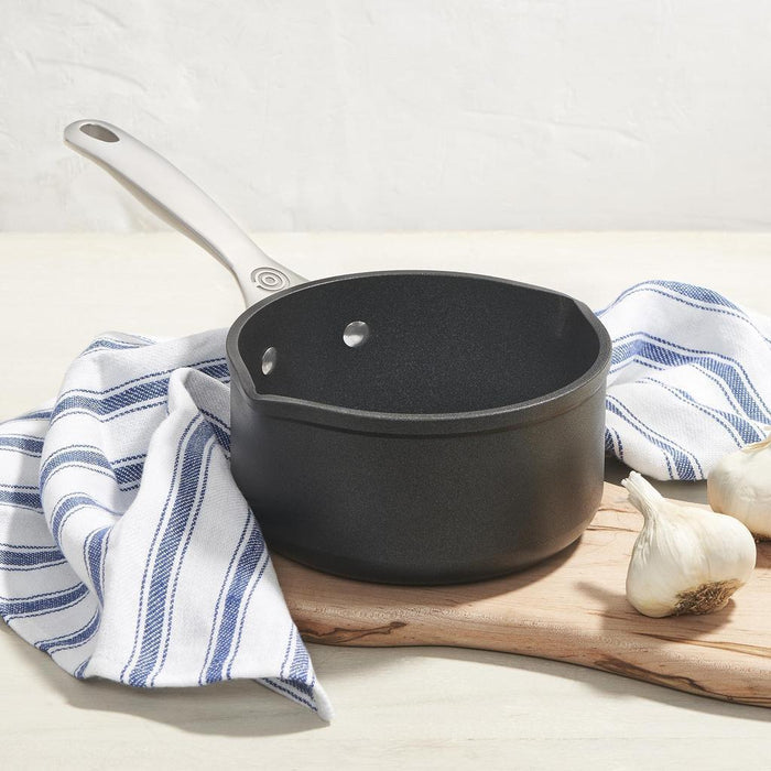 Black saucepan on a wooden cutting board with garlic and a striped cloth