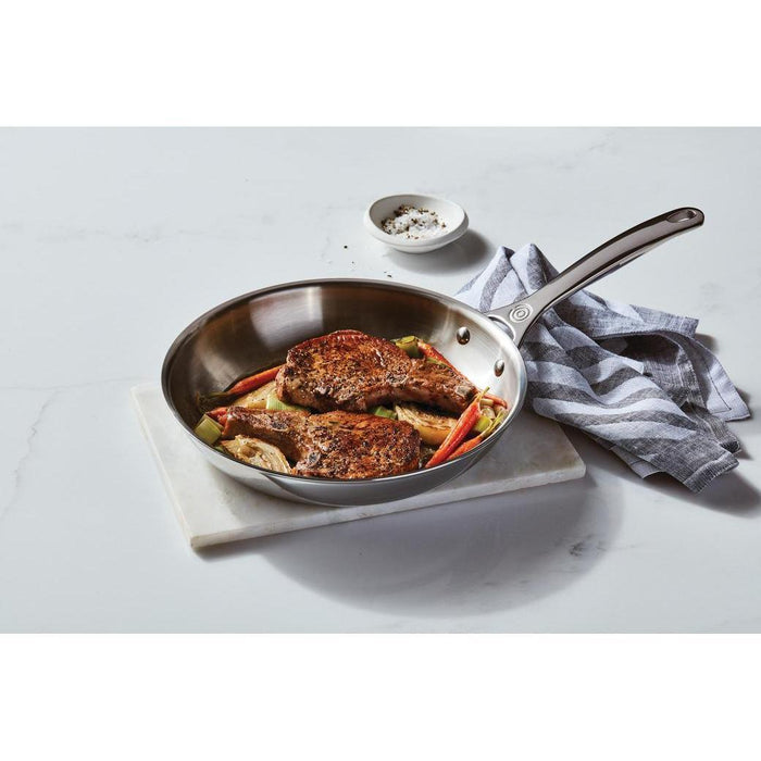 Le Creuset Tri-Ply Stainless Steel Nonstick Fry Pan with cooked vegetables and lamb chops on a white countertop
