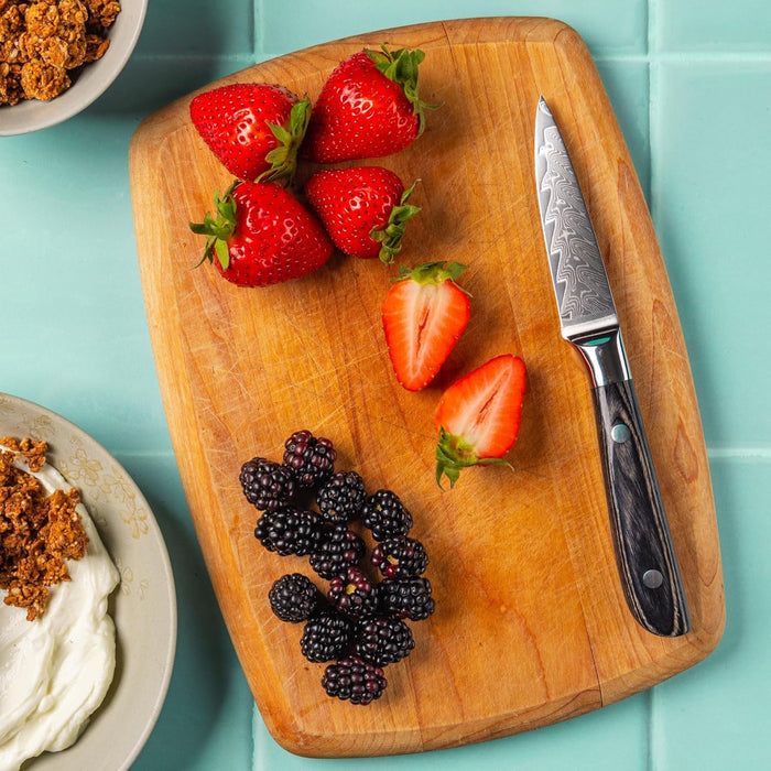 Wooden cutting board with strawberries, blackberries, and a knife on a turquoise background