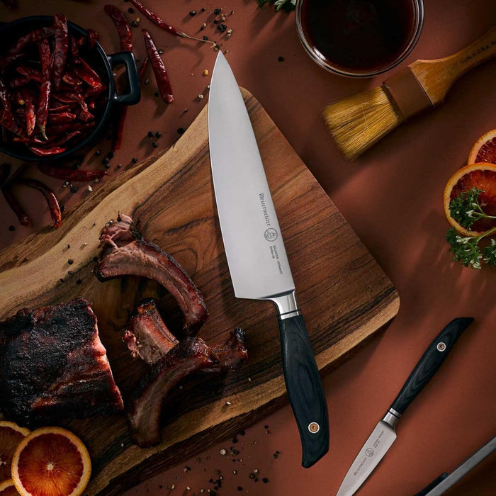 Chef's knife on a wooden cutting board with cooked meat, spices, and a bowl of sauce.
