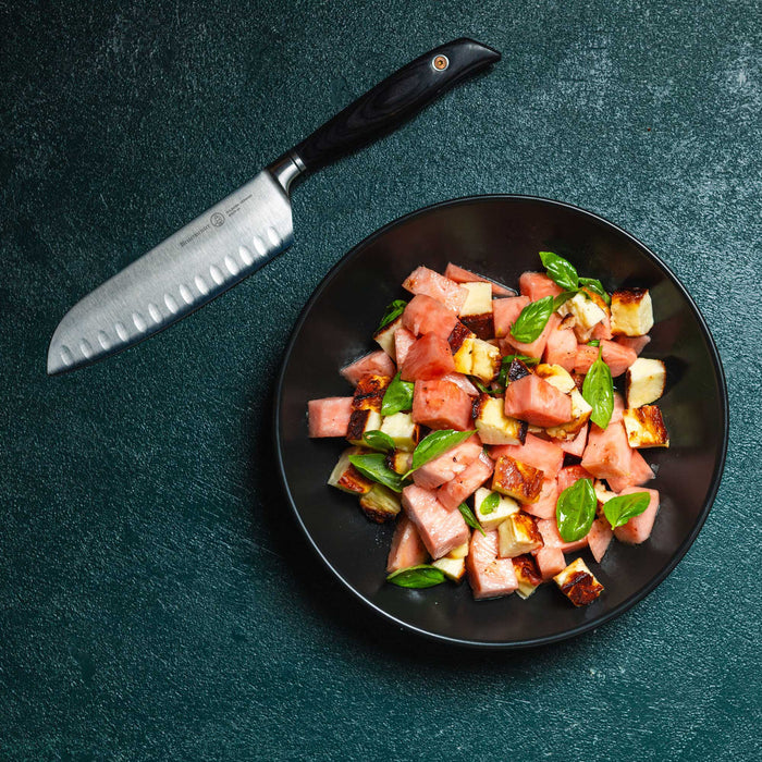 Black plate with watermelon salad and a knife on a dark surface