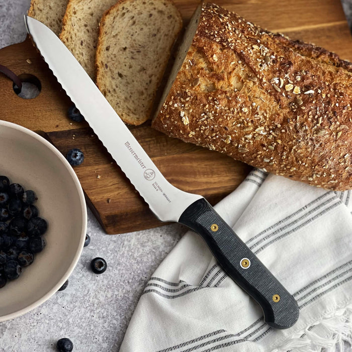 8 inch bread knife next to bread loaf and blueberries on a cutting board displayed on a grey surface