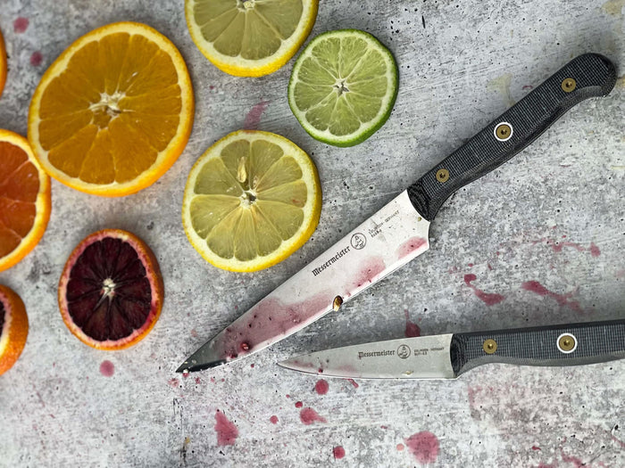 Two knives next to sliced oranges, grapefruit, and limes on a grey surface