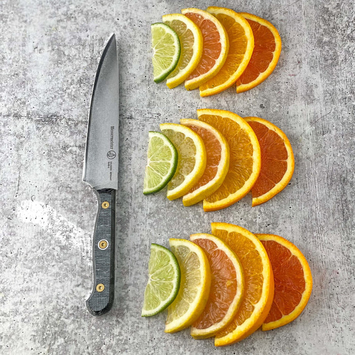 6 inch utility knife next to three rows of sliced oranges, lemons, and limes on a grey surface