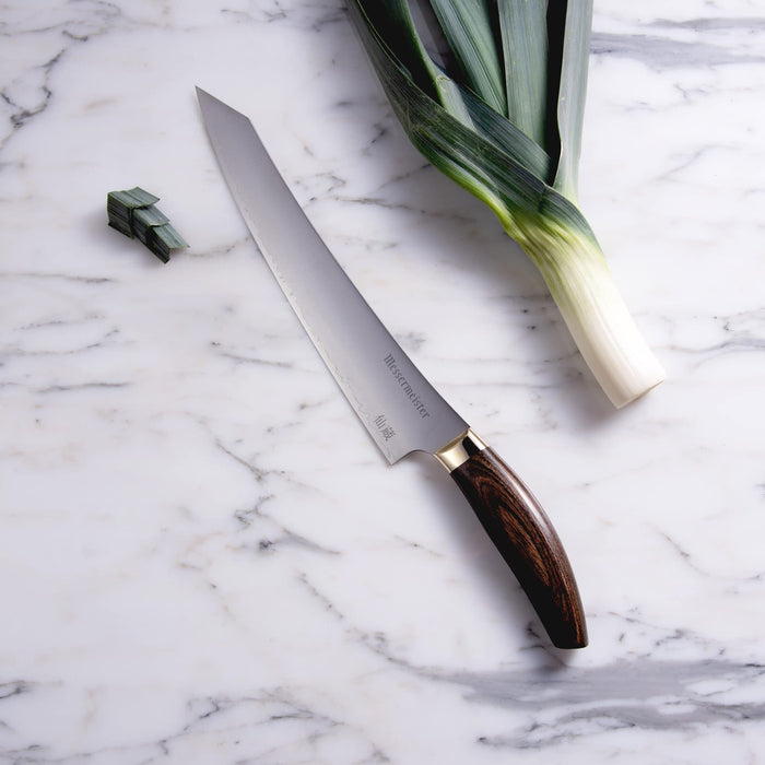 10 inch slicing knife next to leeks displayed on a marble surface